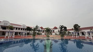 A hotel courtyard with a central pool, surrounded by white buildings with red roofs and palm trees.