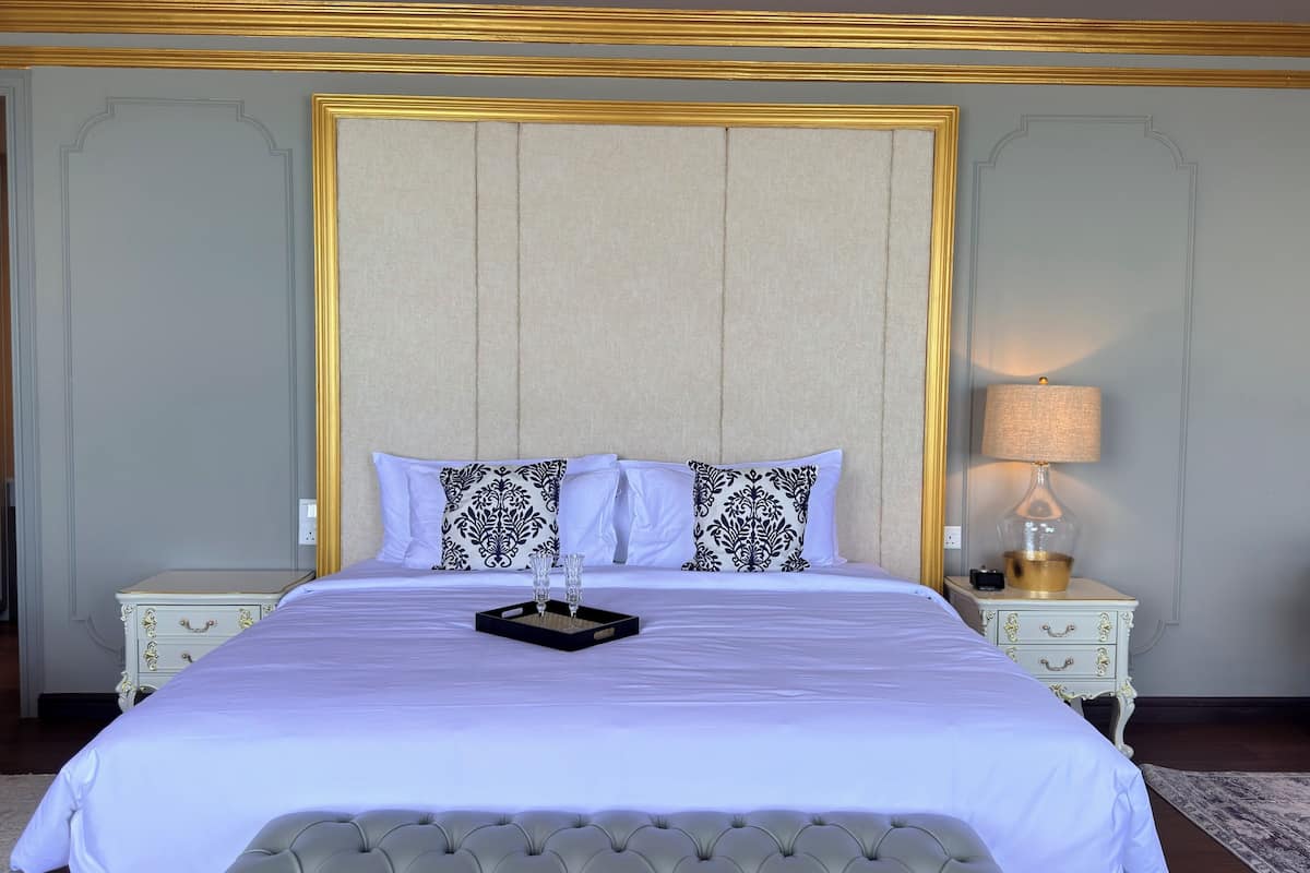 Un grand lit doté d’une tête de lit capitonnée, deux tables de chevet avec des lampes et un coussin à motifs.