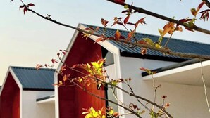 A row of red barns with white walls and a metal roof, surrounded by a concrete pathway and grass. - The Orange Grand Resort (Det Udom)