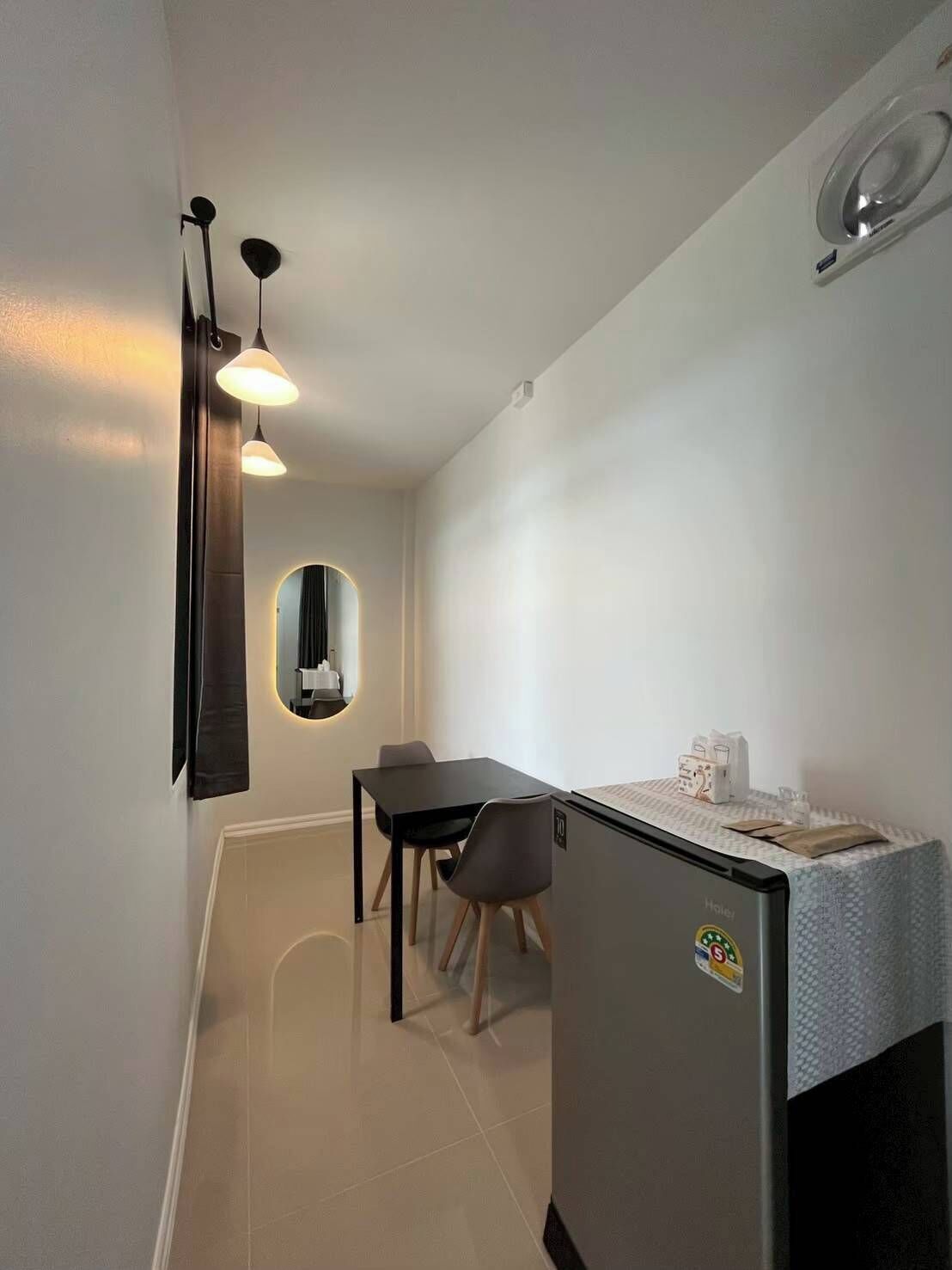 A compact hotel room with a kitchenette, a dining area with a table and chairs, and a mirror with a circular frame.