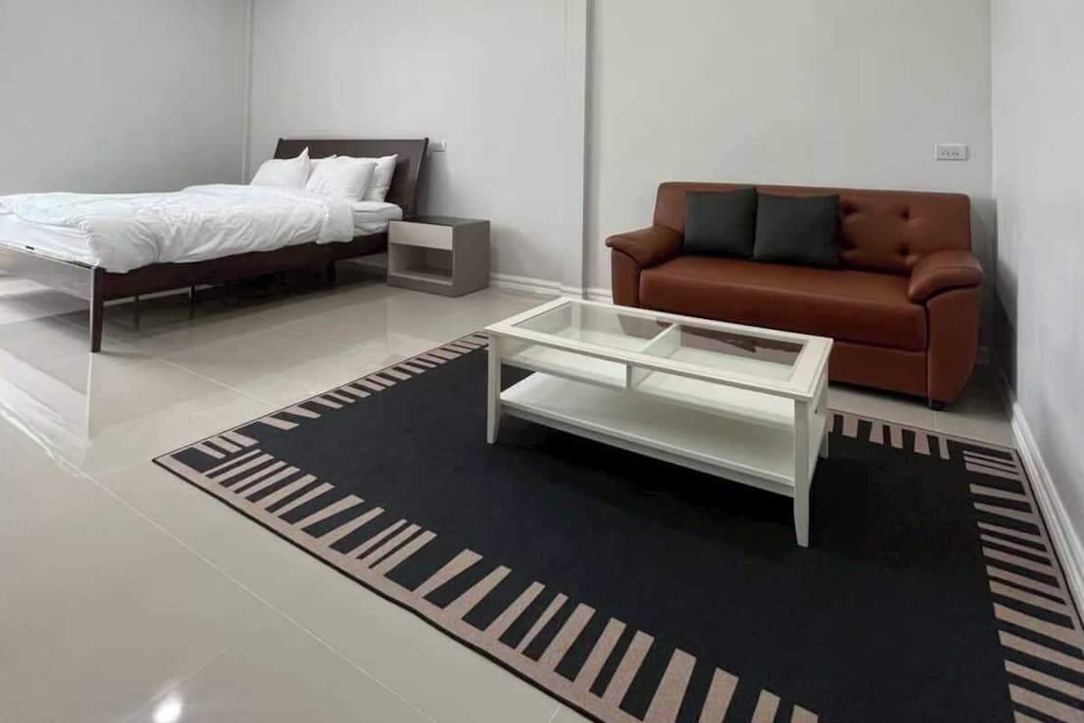 Un dormitorio moderno con una cama, un sofá marrón, una mesita de centro y una alfombra estampada.