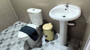 A bathroom with a toilet, a sink, and a trash bin. - The Orange Grand Resort (Det Udom)