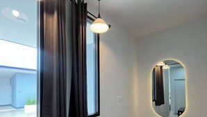 A modern room with a dark table, two pendant lights, a large mirror with a circular frame, and a window with dark curtains. - The Orange Grand Resort (Det Udom)