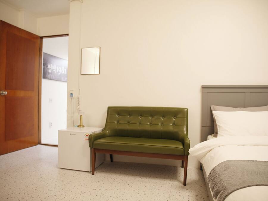 Ett hotellrum med en grön klädd fåtölj, en säng med vita sängkläder och en dörr av trä.