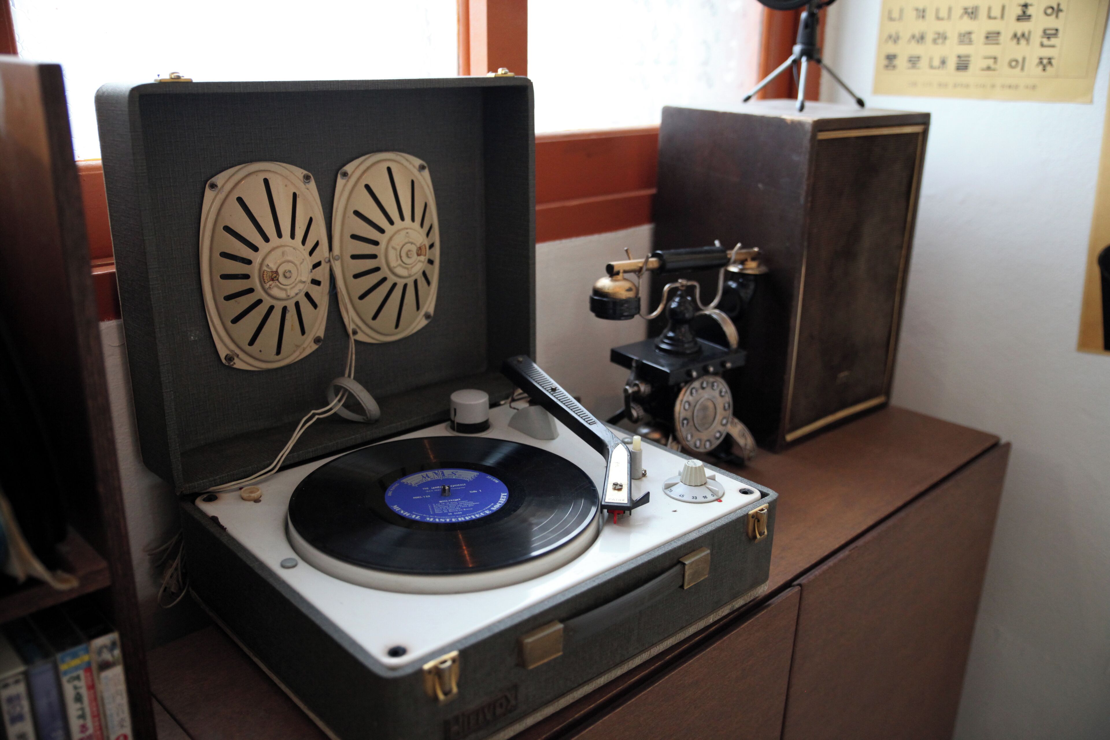 A vintage turntable with two cooling fans, a needle, and a record on a wooden cabinet.