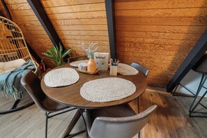 A round wooden table with four chairs, a woven placemat, a welcome sign, a small potted plant, and a container with pencils.