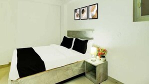 A bedroom with a bed, a nightstand with a lamp, and three framed pictures on the wall. - Hotel Aditya Inn (Jaipur)