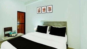 A hotel room with a bed, a nightstand, a wooden door, and three framed pictures on the wall. - Hotel Aditya Inn (Jaipur)