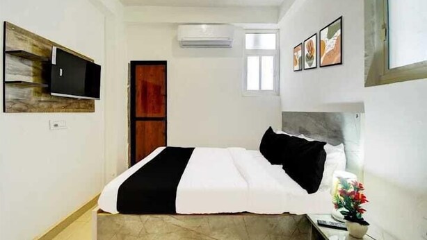 A bedroom with a bed, a TV mounted on a wooden panel, an air conditioning unit, and framed pictures on the wall. - Hotel Aditya Inn (Jaipur)