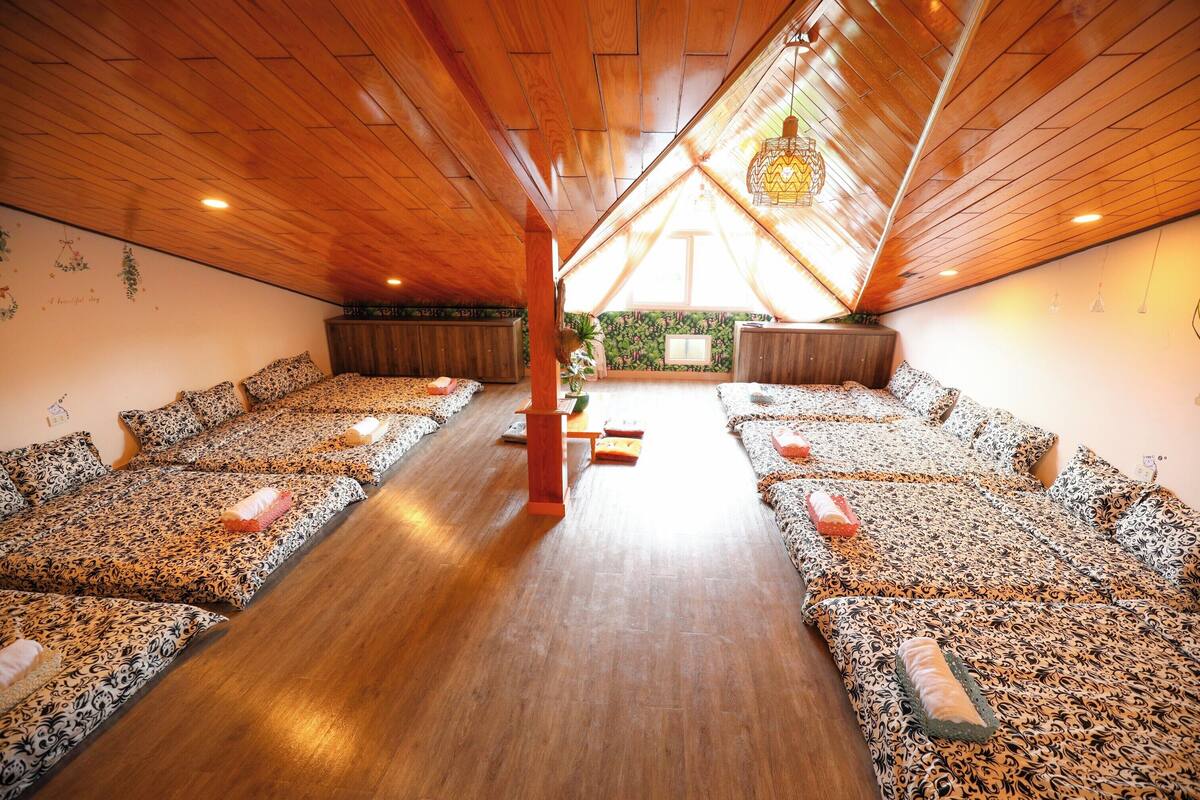 A room with a sloped ceiling, wooden flooring, and multiple beds with patterned bedding.