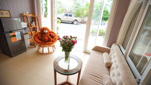 Ein Wohnzimmer mit einer Couch, einem runden Glastisch mit Blumen in einer Vase, einem Korbstuhl und einem Kühlschrank.