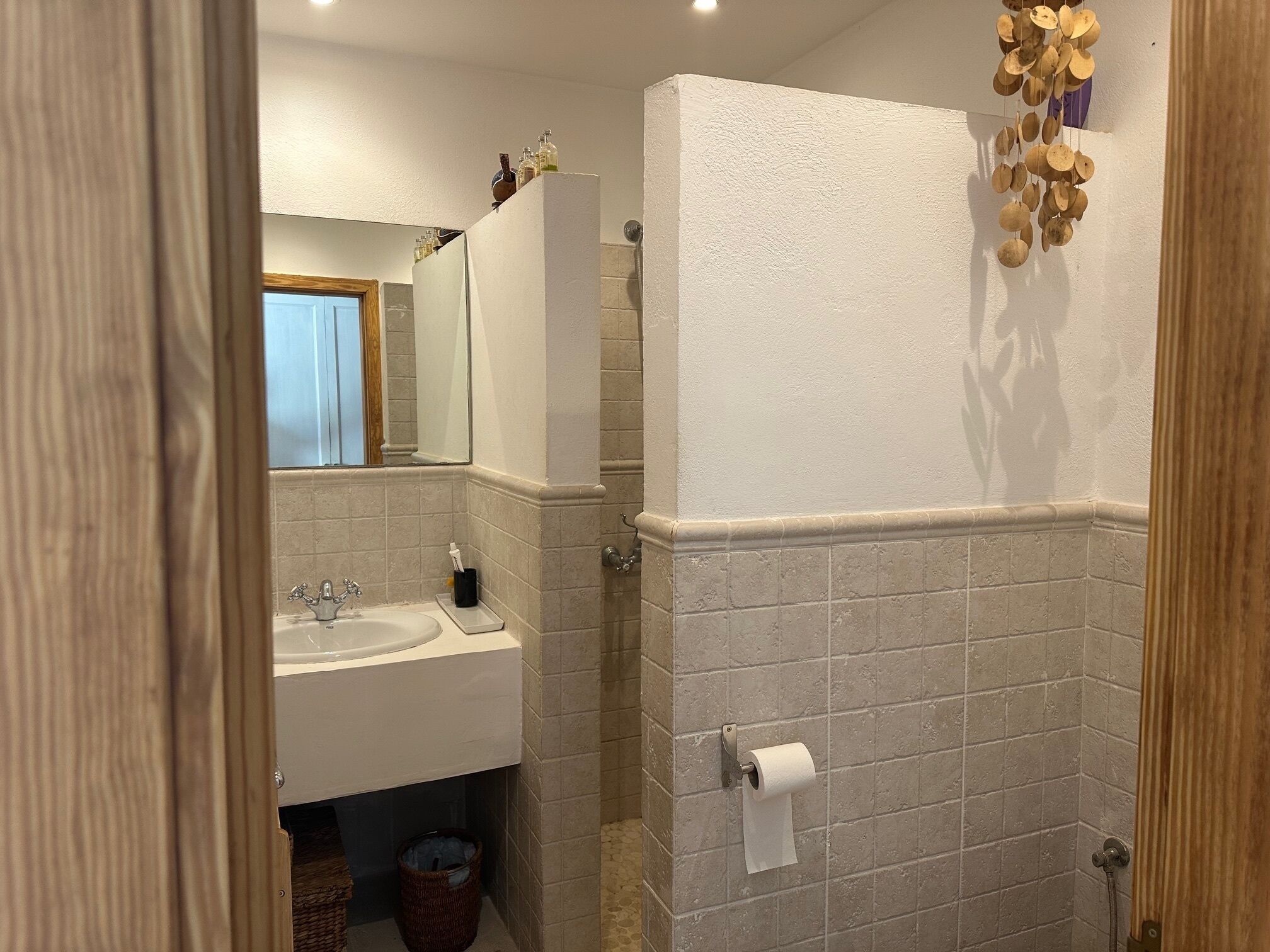 Et badeværelse med håndvask, spejl og toiletpapirsholder.