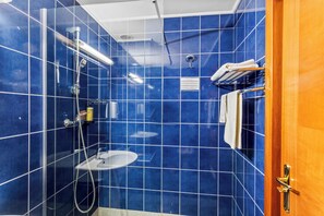 A bathroom with blue tiled walls, a glass shower enclosure, a white sink, and a towel rack with towels.