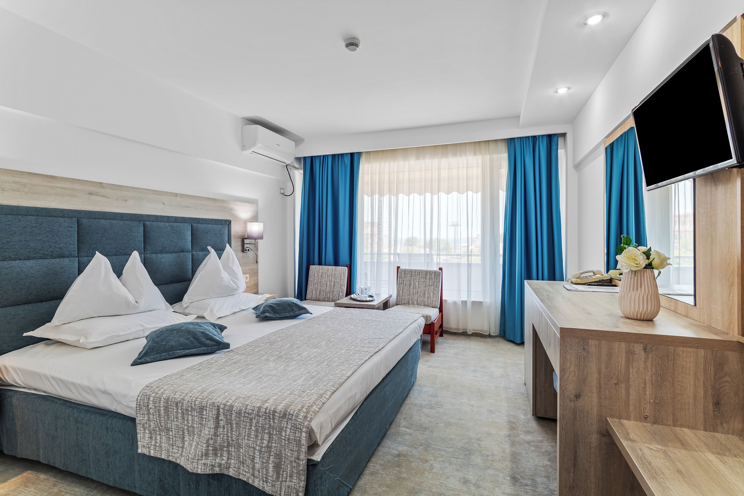 A modern hotel room with a large bed, a desk, and a TV.