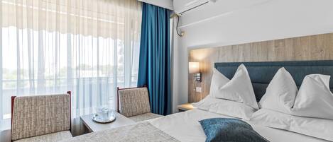A hotel room with a bed, two chairs, a nightstand, and a window with curtains.