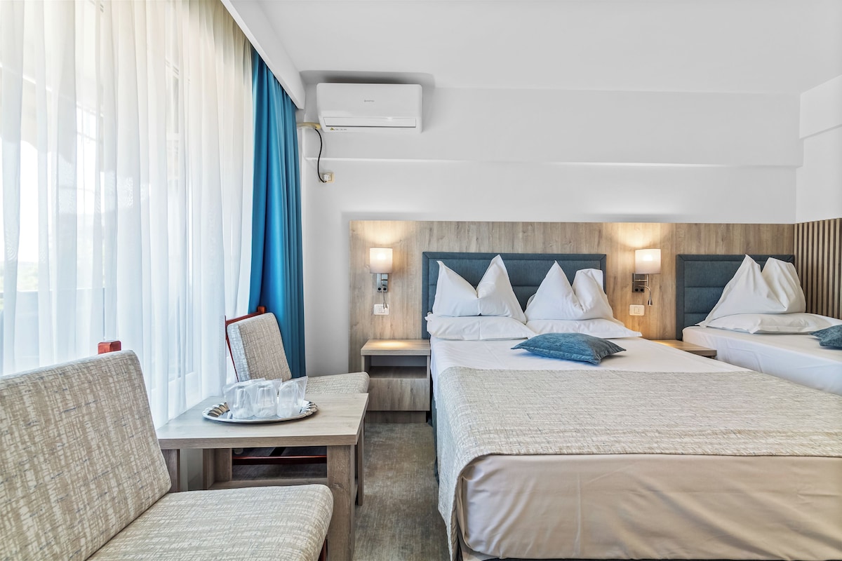 Una habitación de hotel con dos camas, un escritorio, una silla y un ventanal con cortinas.
