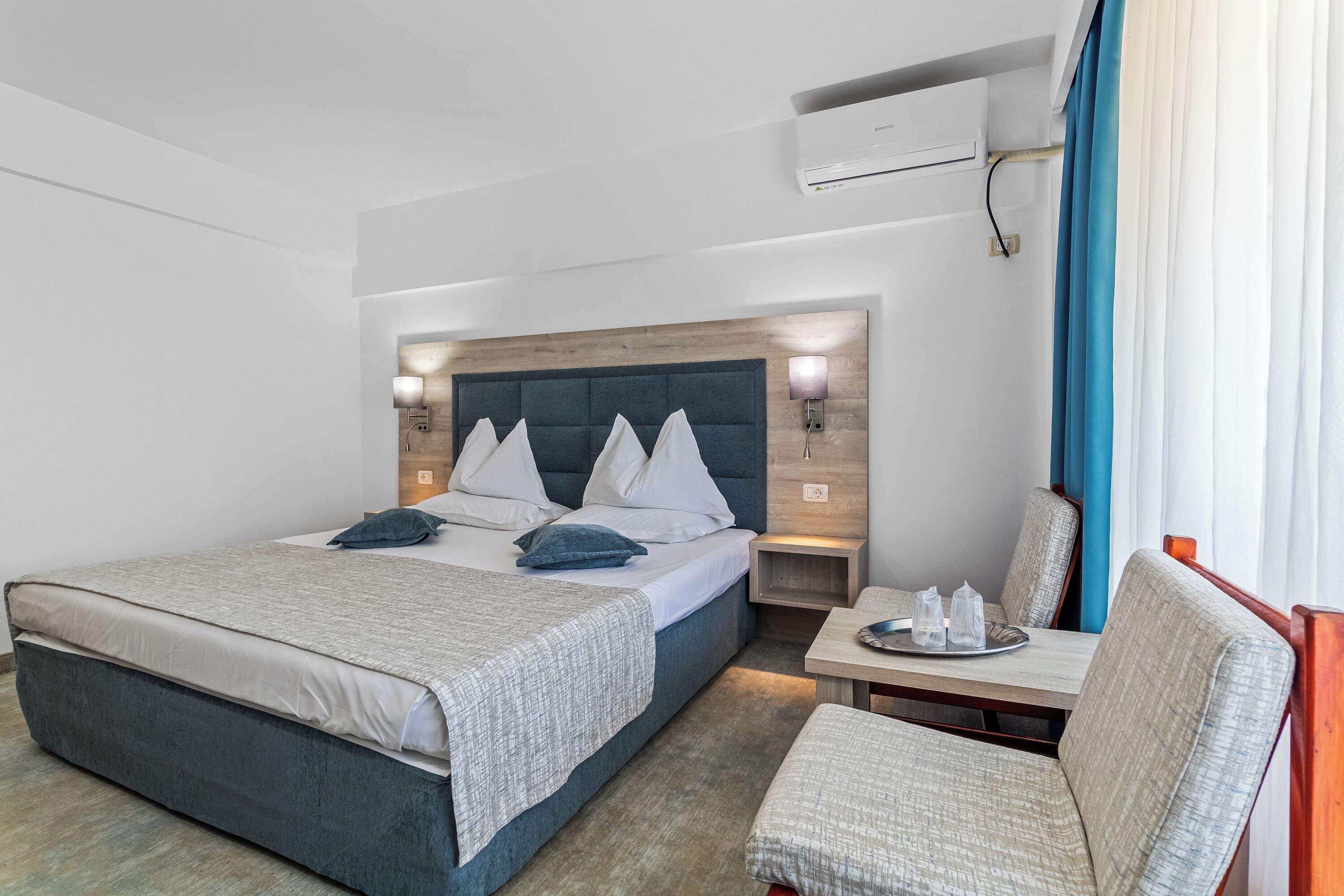 A modern hotel room with a large bed, bedside tables, a small table with a tray, and a chair.