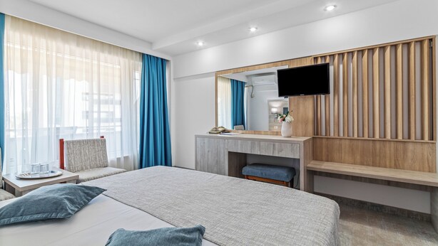 A modern hotel room with a large bed, a desk with a flat-screen TV, a mirror, and a window with blue curtains. - Hotel Condor (Constanta)