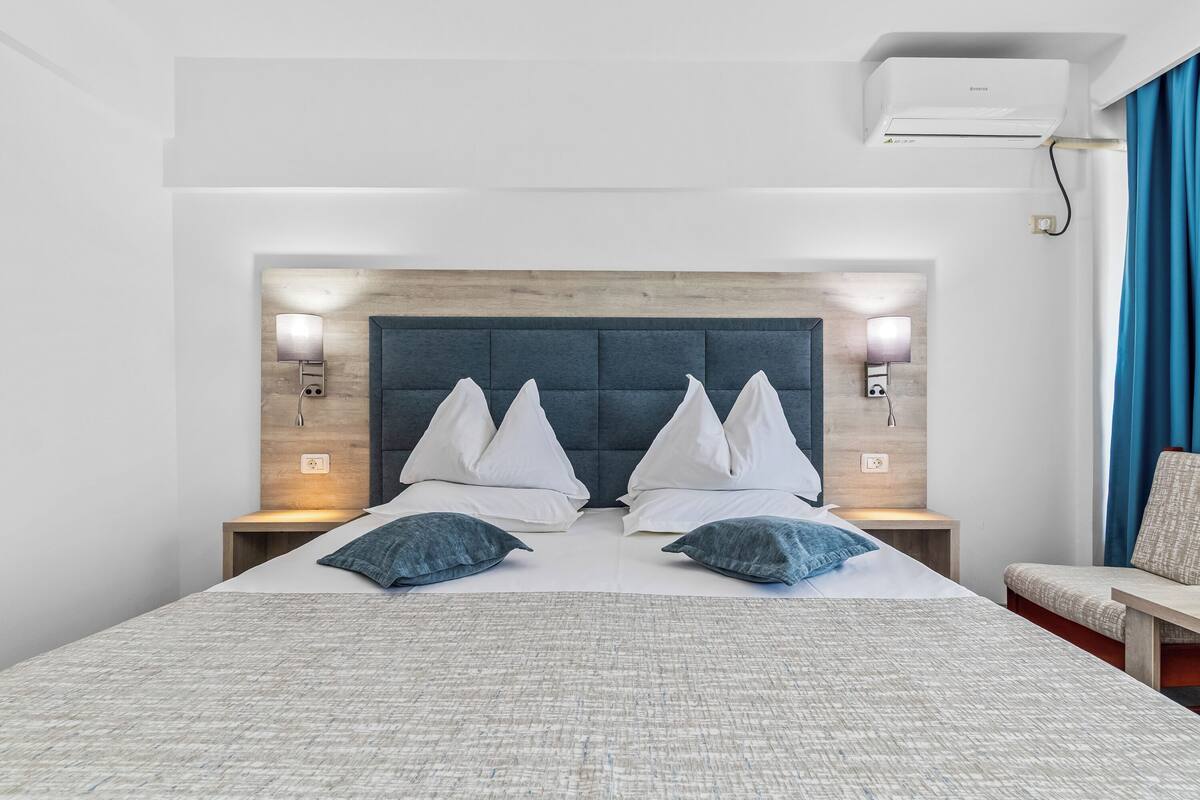Une chambre d’hôtel avec un grand lit, une tête de lit en bois, des lampes de chevet et un climatiseur fixé au plafond.