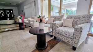 A modern lobby with patterned sofas, a round table with a vase of flowers, and large windows offering a view of greenery outside. - Hotel Condor (Constanta)
