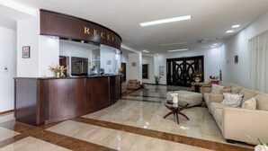 A reception area with a wooden reception desk, a sofa, and a coffee table. - Hotel Condor (Constanta)