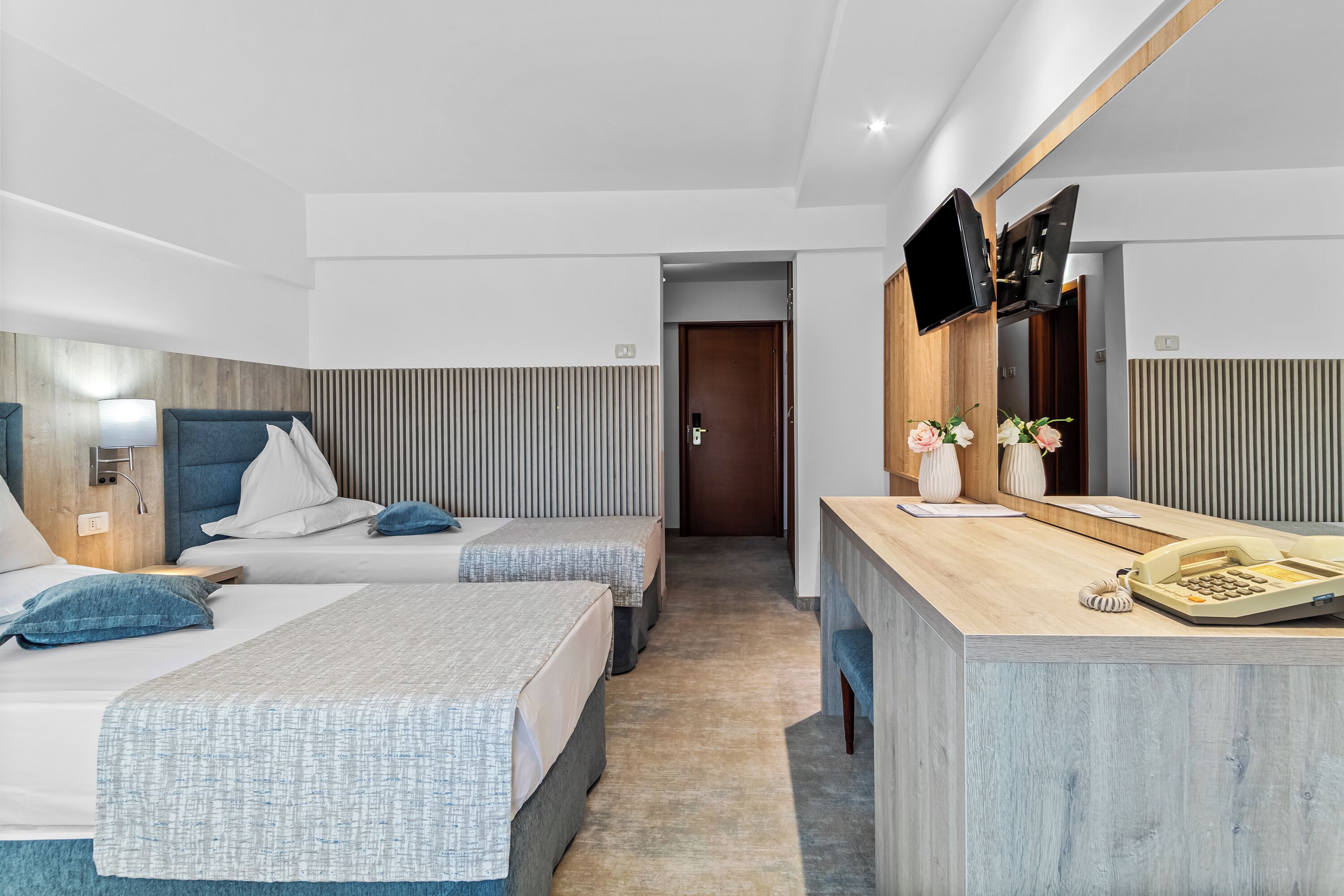 A modern hotel room with two beds, a desk with a telephone, and a TV mounted on the wall.