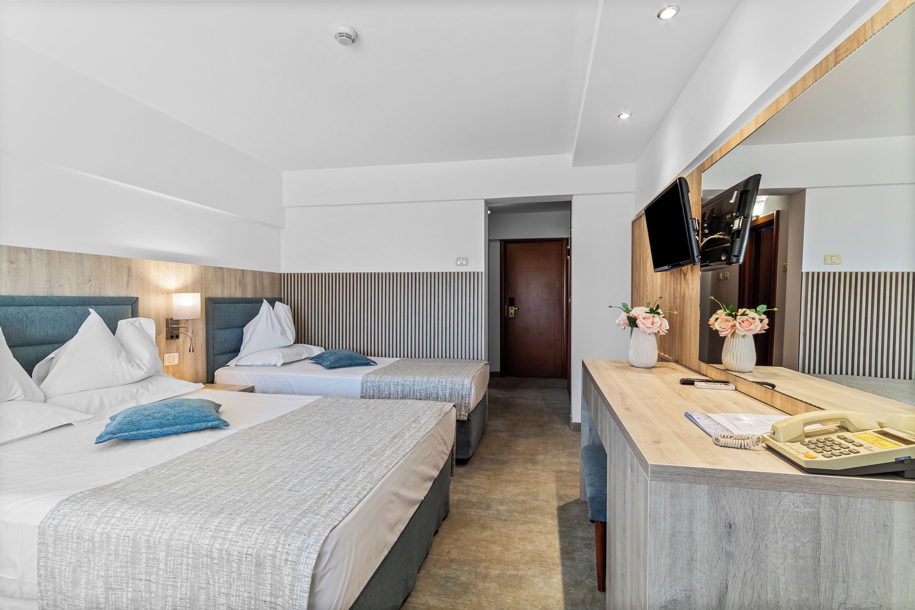 Une chambre d’hôtel avec deux lits, un bureau avec un téléphone et un téléviseur fixé au mur.