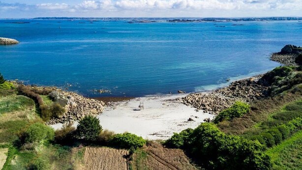 Een kustlandschap met een zandstrand, een rotsachtige kustlijn en een helder uitzicht op de zee.