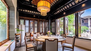 A traditional-style dining room with a round table, chairs, and a large window offering a view of a traditional building. - Suzhou Shantang Scholars Boutique Hotel (Suzhou)