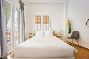 A bedroom with a large bed, a window with decorative bars, a chair, and a nightstand with a lamp. - Stylish Apartment in Thissio | Dedicated Workspace (Athina)