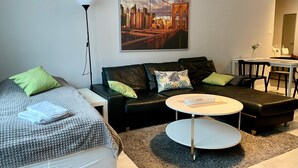 A modern living room with a sofa set, a coffee table, and a painting of a bridge. - Kotimaailma KotikolmioOikokatu (Lahti)