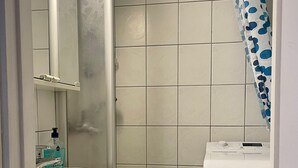 A bathroom with a white sink, a mirror, a toilet, and a shower with a blue polka dot shower curtain. - Kotimaailma KotikolmioOikokatu (Lahti)