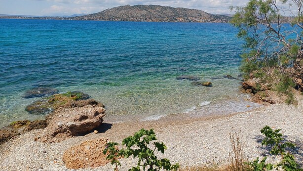 A clear view of a pebble beach with a rocky outcrop and sparse vegetation. - Villa Mariza at Aiantio (Salamina)