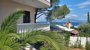 A two-story building with a balcony, surrounded by greenery and a view of the sea. - Villa Mariza at Aiantio (Salamina)