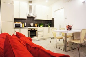 Een moderne keuken met witte kasten, een magnetron en een eethoek met een tafel en stoelen.