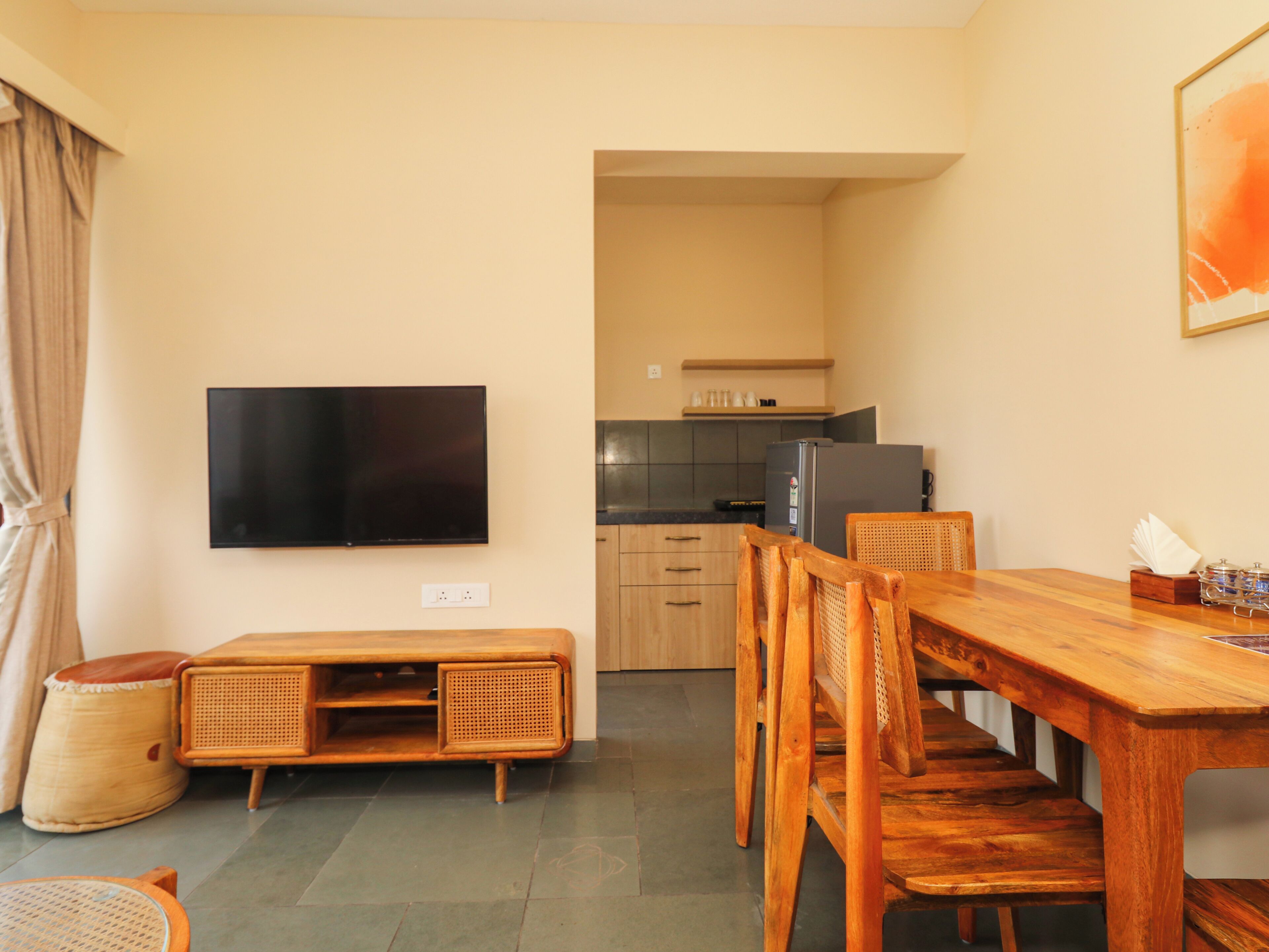 A compact living space with a dining area, kitchenette, and a flat-screen TV mounted on the wall.
