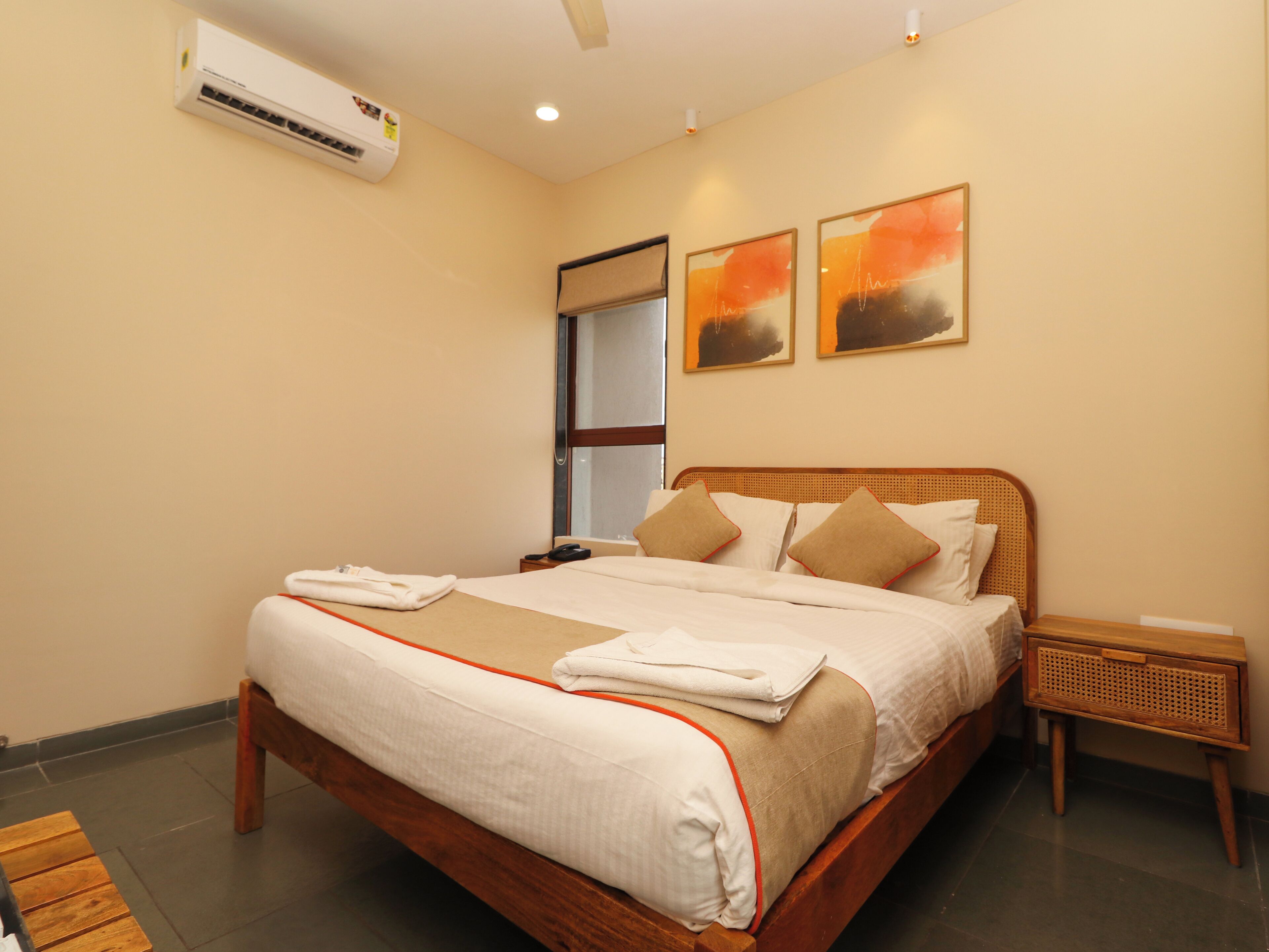 A neatly made bed with white linens and orange trim, a wooden headboard, and a bedside table with a lamp.
