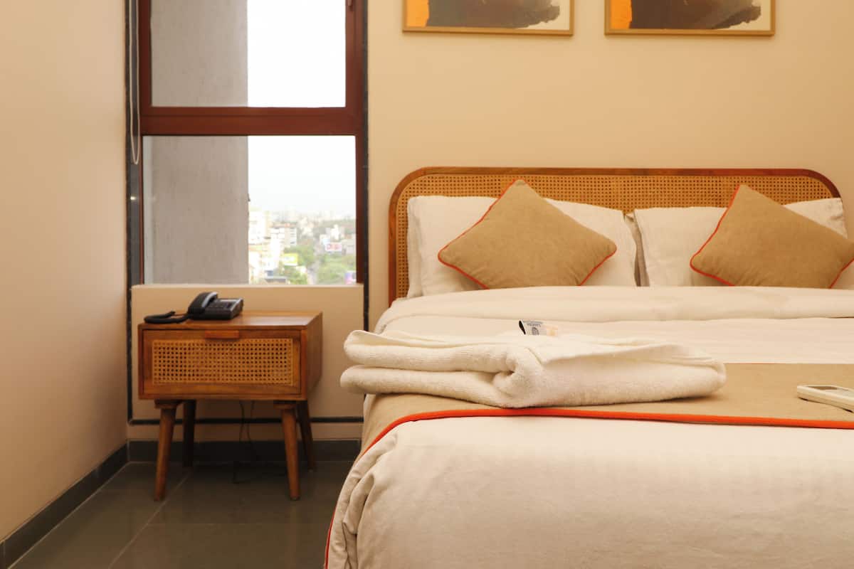 A hotel room with a bed, a bedside table with a phone, and a window with a city view.