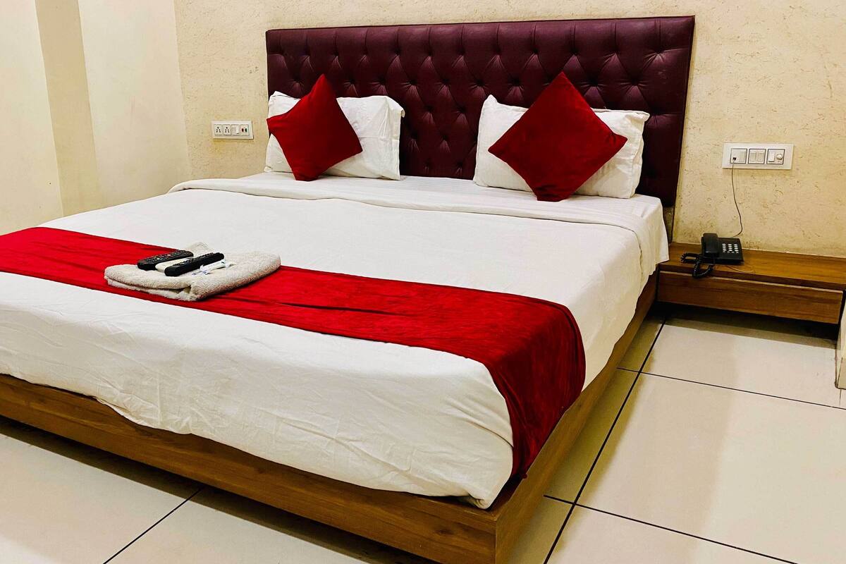 A neatly made bed with a red and white bedspread, two red and white pillows, and a remote control on the bed.