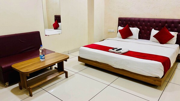 Une chambre d’hôtel avec un lit, une table en bois, une bouteille d’eau et un oreiller rouge.