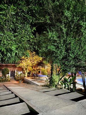Ein tropisches Resort mit Pool, Liegestühlen und strohgedeckten Gebäuden.