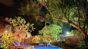 A nighttime pool area with lounge chairs and a thatched-roof structure. - Alfa Kuta (Kuta)