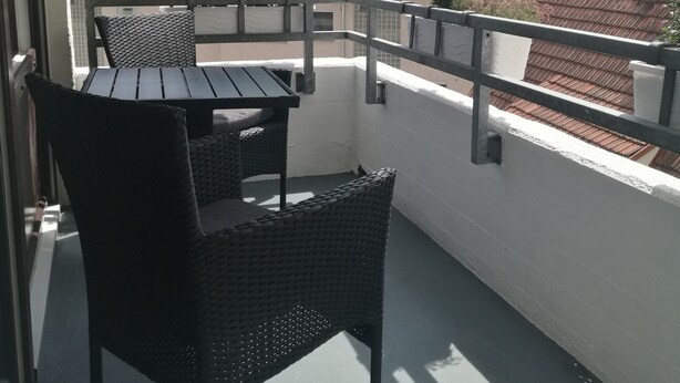 Een balkon met een tafel en stoelen, met uitzicht op een woongebied met rode pannendaken en groen.