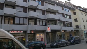 Een meerlaags gebouw met een apotheek op de begane grond, een zichtbaar bord voor een kapsalon, en meerdere geparkeerde auto's.