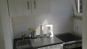 Een compacte keuken met witte kasten, een zwart aanrecht, een spoelbak, een koffiezetapparaat en een fornuis.
