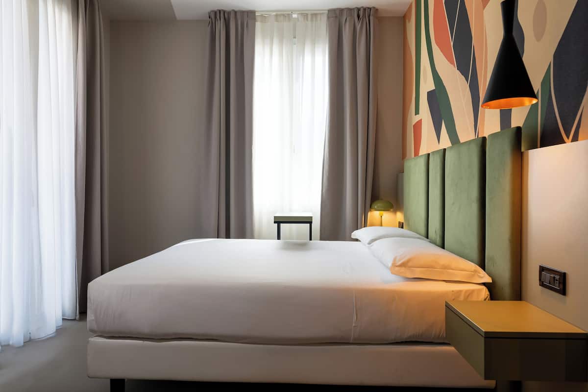 A hotel room with a large bed, a bedside table, a lamp, and a wall with abstract art.