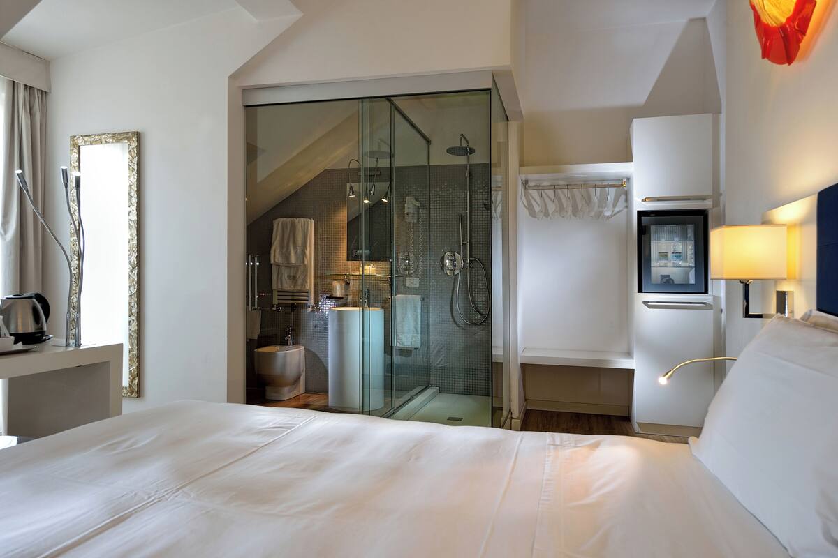 A hotel room with a large bed, a glass-enclosed shower area, a small bathroom, and a minibar.