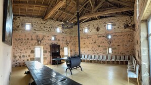 A rustic room with stone walls, wooden beams, a long table, chairs, and mounted animal heads. - Le Gîte de Font Valet (Millac)