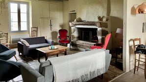 A living room with a stone fireplace, a sofa, a red chair, and a wooden table. - Le Gîte de Font Valet (Millac)