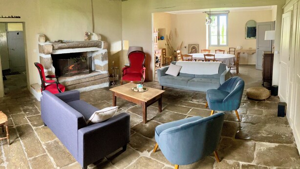 A rustic living room with stone flooring, a fireplace, a blue sofa, and a red armchair. - Le Gîte de Font Valet (Millac)